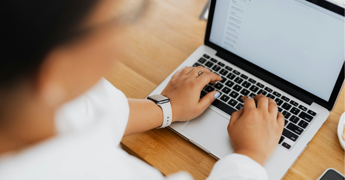 A laptop sits on a desk while someone places their hands on the keyboard.